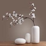 Une branche de fleurs de cerisier blanche épanouie dans un vase en céramique aux formes simples et épurées, créant une composition zen et élégante.