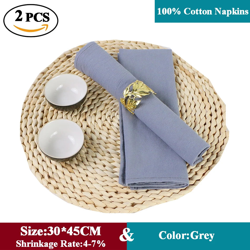 Serviettes de table en coton gris sur un tapis de table en paille tressée, avec deux bols en céramique blanche et un anneau de serviette décoratif.