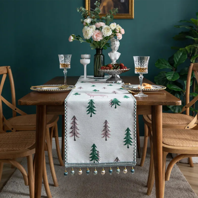 Une table d'hiver élégante avec un bouquet de fleurs fraîches, des verres à vin et une nappe ornée de pins verts.