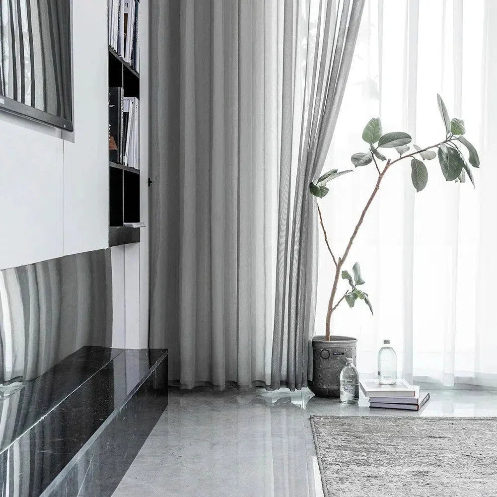 Intérieur moderne et épuré avec des rideaux gris élégants. Plante en pot ajoutant une touche naturelle à la pièce. Le sol brillant et le tapis doux créent une ambiance sophistiquée. Étagères remplies de livres apportant une dimension culturelle à l'espace de vie.