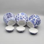 Trois vases décoratifs en porcelaine blanche et bleue, ornés de motifs floraux et de symboles asiatiques, sur un fond gris.