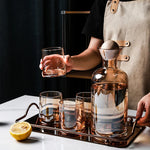Une magnifique carafe en verre transparent avec des verres assortis, accompagnée d'un citron, sur un plateau argenté, représentant un élégant ensemble de service pour les boissons.