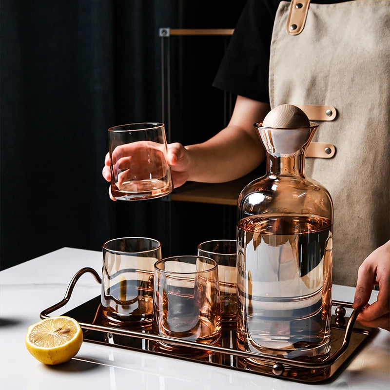 Une magnifique carafe en verre transparent avec des verres assortis, accompagnée d'un citron, sur un plateau argenté, représentant un élégant ensemble de service pour les boissons.