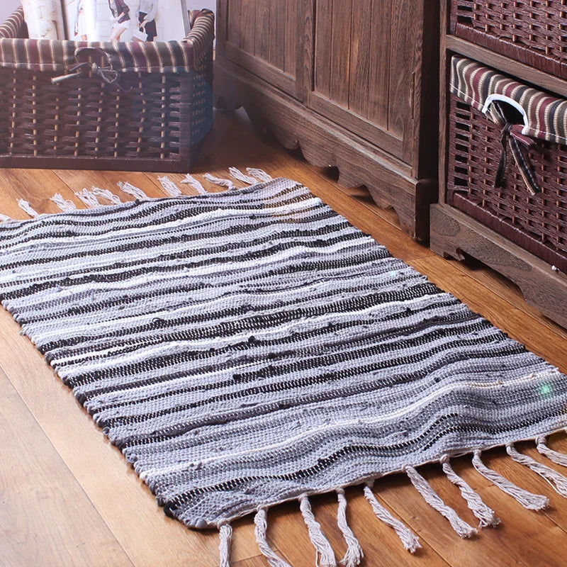 Un tapis rayé en noir et blanc, aux franges pendantes, décorant le sol d'un espace intime et rustique.