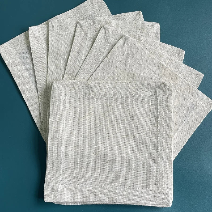 Pile de serviettes de table en lin beige sur fond vert foncé.