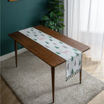 Une table en bois foncé avec une nappe motif arbres et montagnes se trouve dans une pièce à décor vert et blanc.