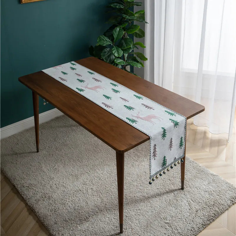 Une table en bois foncé avec une nappe motif arbres et montagnes se trouve dans une pièce à décor vert et blanc.