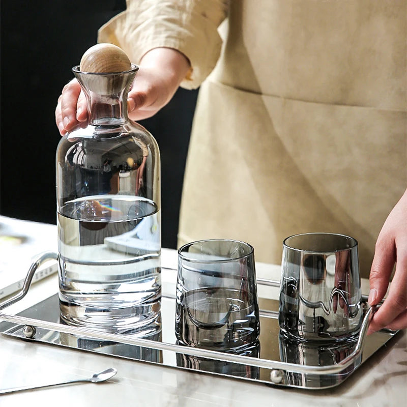 Une bouteille et des verres de cristal sur un plateau en métal brillant, avec une personne portant un tablier blanc à la main.