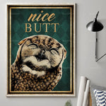 Un gros plan sur le visage d'un oiseau aux plumes dorées et brunes, avec le texte "Nice Butt" en lettrage doré sur un fond vert foncé dans un cadre décoratif.