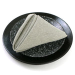 Sur un plat noir et brillant, un linge en lin beige, soigneusement plié en forme de triangle, ajoute une touche d'élégance minimaliste à cette mise en scène.