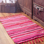 Un tapis en coton multicolore avec des rayures rose vif sur le sol en bois, complété par des paniers en osier.