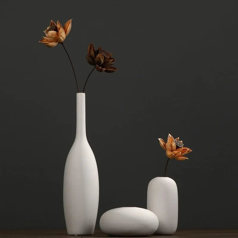 Trois vases blancs minimalistes contenant des fleurs en bronze au style élégant et épuré, sur fond noir.