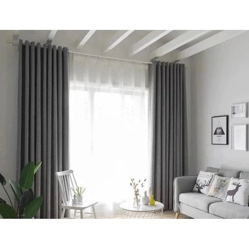 Image d'un salon moderne et élégant avec des rideaux gris foncé, illuminé par une lumière naturelle douce provenant de la fenêtre. Le décor est complété par un canapé confortable avec des coussins illustrés et une table basse design, offrant un style contemporain et chaleureux pour un espace de vie raffiné.