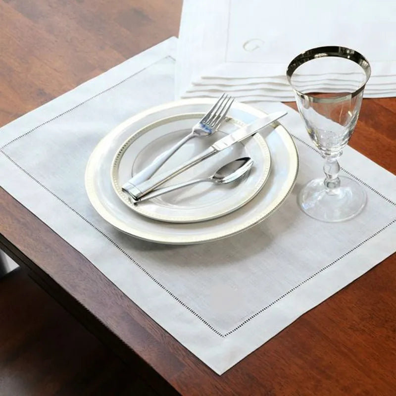 Une table dressée avec des assiettes, des couverts et un verre de vin, sur un set de table blanc.