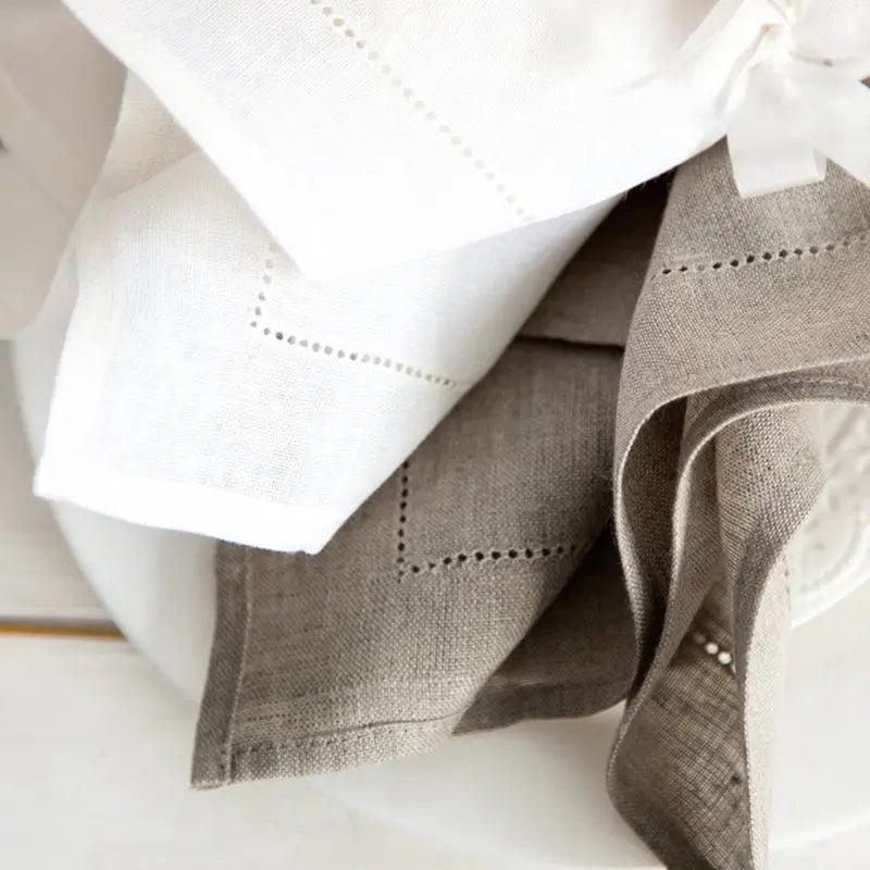 Des serviettes de table en lin blanc et gris avec de délicats points de broderie décorative, dégageant une atmosphère élégante et raffinée dans la cuisine ou la salle à manger.