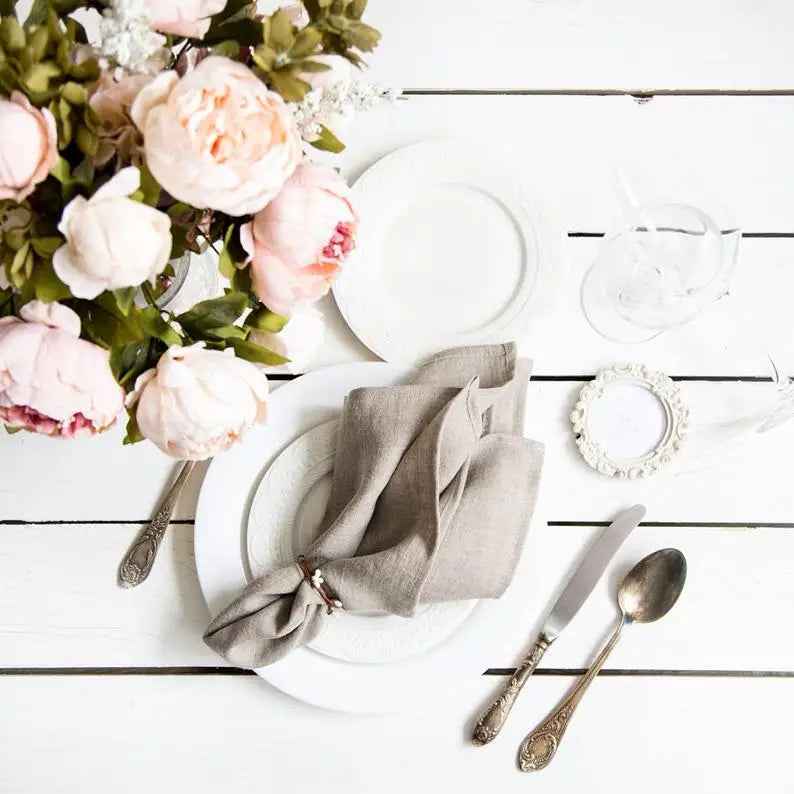 Une table élégante avec des roses roses, des assiettes blanches et une serviette en lin beige, entourée de couverts vintage.