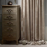 Commode vintage à cinq tiroirs avec motifs sculptés, placée à côté de rideaux élégants tombant gracieusement jusqu'au sol. Idéale pour apporter une touche de charme classique à votre intérieur, cette commode offre un espace de rangement pratique tout en rehaussant la décoration de la pièce.