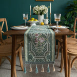 L'image présente une table de salle à manger élégamment décorée avec des fleurs, des bougies, des verres de cristal et une belle nappe ornée de motifs floraux.