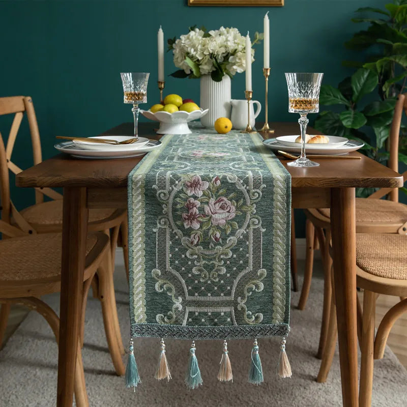 L'image présente une table de salle à manger élégamment décorée avec des fleurs, des bougies, des verres de cristal et une belle nappe ornée de motifs floraux.