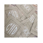 Pile de serviettes de table beige avec des motifs blancs qui semblent être des initiales ou un logo.