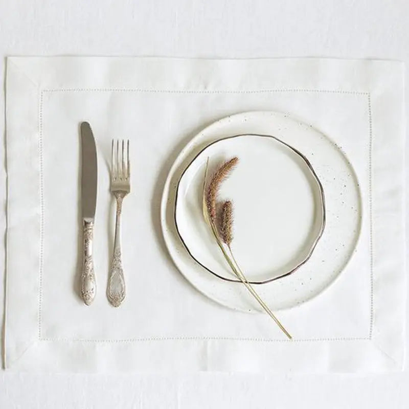 Sur une nappe blanche se trouvent une assiette et des couverts, ainsi qu'un élément décoratif naturel évoquant les plumes.