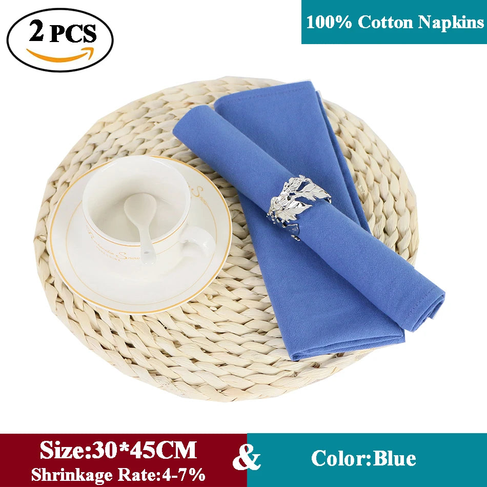 Deux serviettes en coton 100% de couleur bleue, de taille 30 x 45 cm, avec un faible taux de rétrécissement de 4 à 7%, posées sur un dessous de plat en osier tressé.