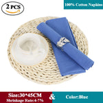 Deux serviettes en coton 100% de couleur bleue, de taille 30 x 45 cm, avec un faible taux de rétrécissement de 4 à 7%, posées sur un dessous de plat en osier tressé.