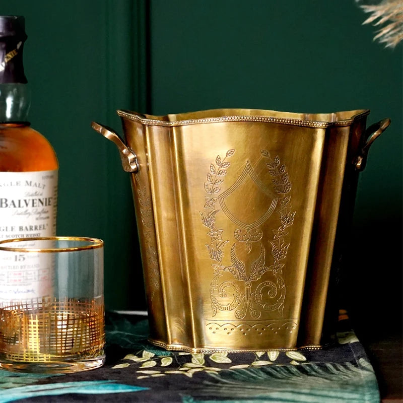 Une coupe dorée ornée de motifs raffinés, accompagnée d'une bouteille de whisky malt sur un fond vert foncé, évoquant un élégant arrangement de produits de luxe.