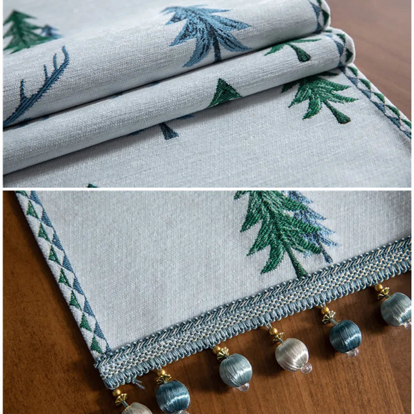 Tissu gris orné de motifs d'arbres verts et bleus stylisés, avec une frange décorative composée de perles métalliques.