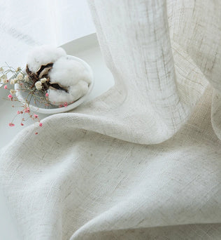 Rideaux élégamment drapés en lin et laine, démontrant l'art créatif du tissage. Les rideaux en matériaux naturels, affichent des nuances subtiles de couleurs pastel. Parfaits pour ajouter une touche cosy et artistique à toute pièce. Ce textile d'ameublement naturel sert également de toile de fond pour une table habillée d'une nappe en lin et entourée de serviettes assorties, soulignant l'importance du lin et de la laine dans la création d'intérieurs confortables et esthétiquement agréables.