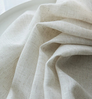 Vue rapprochée d’un tissu de voilage beige effet lin naturel, délicatement froissé, mettant en valeur sa texture douce et sa transparence.