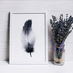 Une délicate plume en noir et blanc encadrée sur un mur en bois, avec un bouquet de lavande dans un vase vintage orné de dentelle.