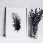 Une plume noire de style artistique, entourée d'un bouquet de lavande violette dans un vase en verre sur une surface en bois.