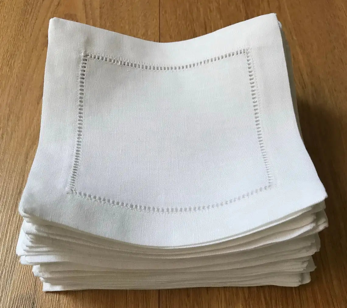 Serviettes en coton blanc avec bordure brodée, pliées en pile sur une surface en bois.
