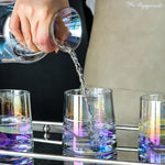 L'image montre un barman versant un liquide coloré dans des verres transparents, créant un effet visuel intéressant avec les reflets et les couleurs.