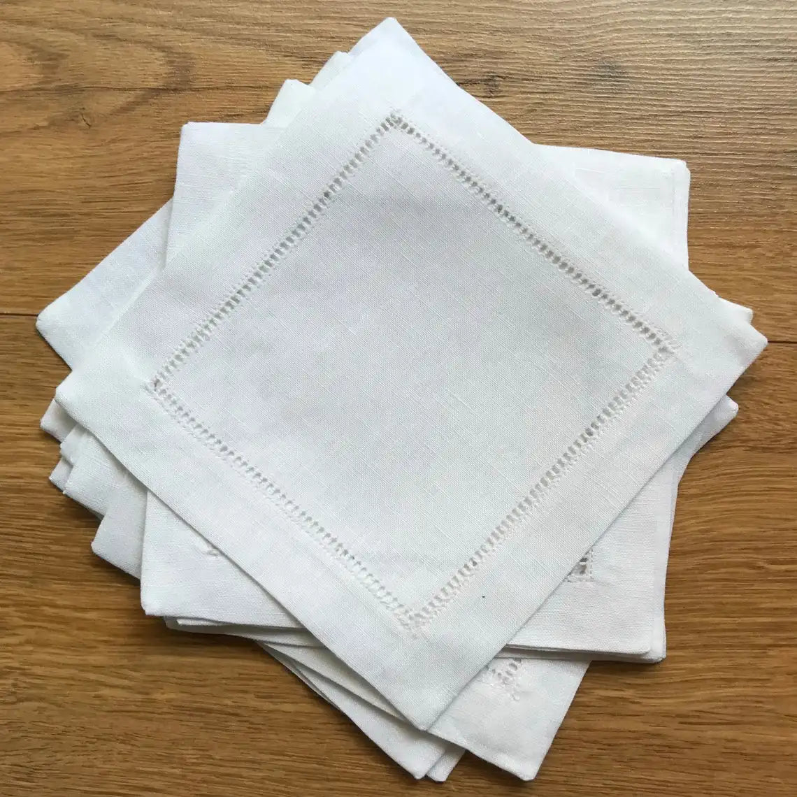 Un ensemble de serviettes de table en tissu blanc, ornées de points de broderie délicats, posées sur une surface en bois.