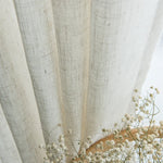 Gros plan sur un voilage effet lin naturel légèrement plissé, accompagné de fleurs séchées blanches pour une ambiance poétique.