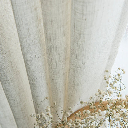 Gros plan sur un voilage effet lin naturel légèrement plissé, accompagné de fleurs séchées blanches pour une ambiance poétique.