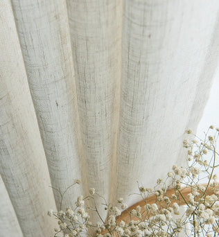 Gros plan sur un voilage effet lin naturel légèrement plissé, accompagné de fleurs séchées blanches pour une ambiance poétique.