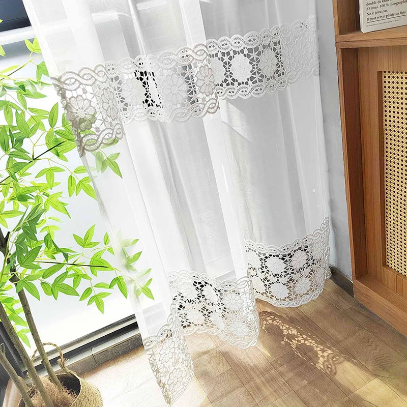 Voilage brodé illuminé par le soleil sur un sol en parquet clair, à côté d’un feuillage vert.