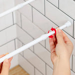 Installation manuelle d'une tringle à rideaux blanche sans perçage sur carrelage, avec rotation pour ajustement.