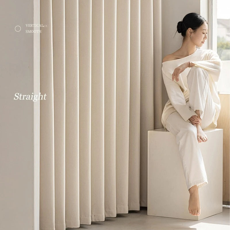 Femme en tenue claire assise près d’un rideau crème fluide et vertical, style épuré et contemporain