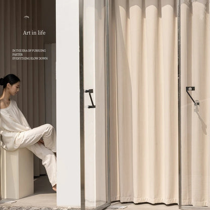 Rideau crème installé sur une baie vitrée avec une femme en tenue blanche, éclairage naturel et décor minimaliste