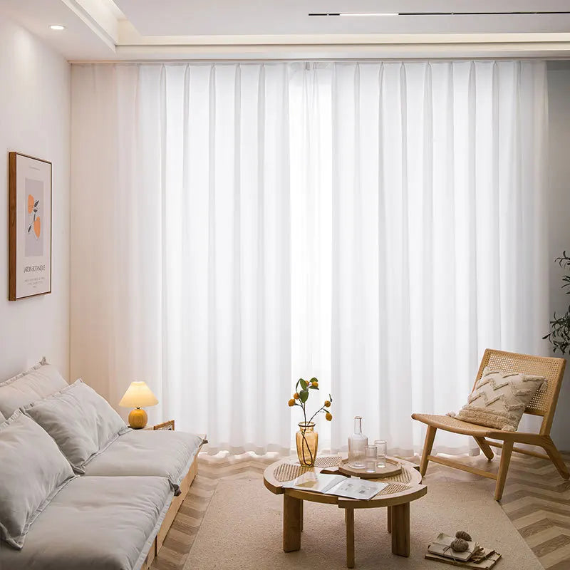Vue d’ensemble d’un salon chaleureux avec de longs voilages blancs installés au plafond sur rail, offrant un éclairage naturel.