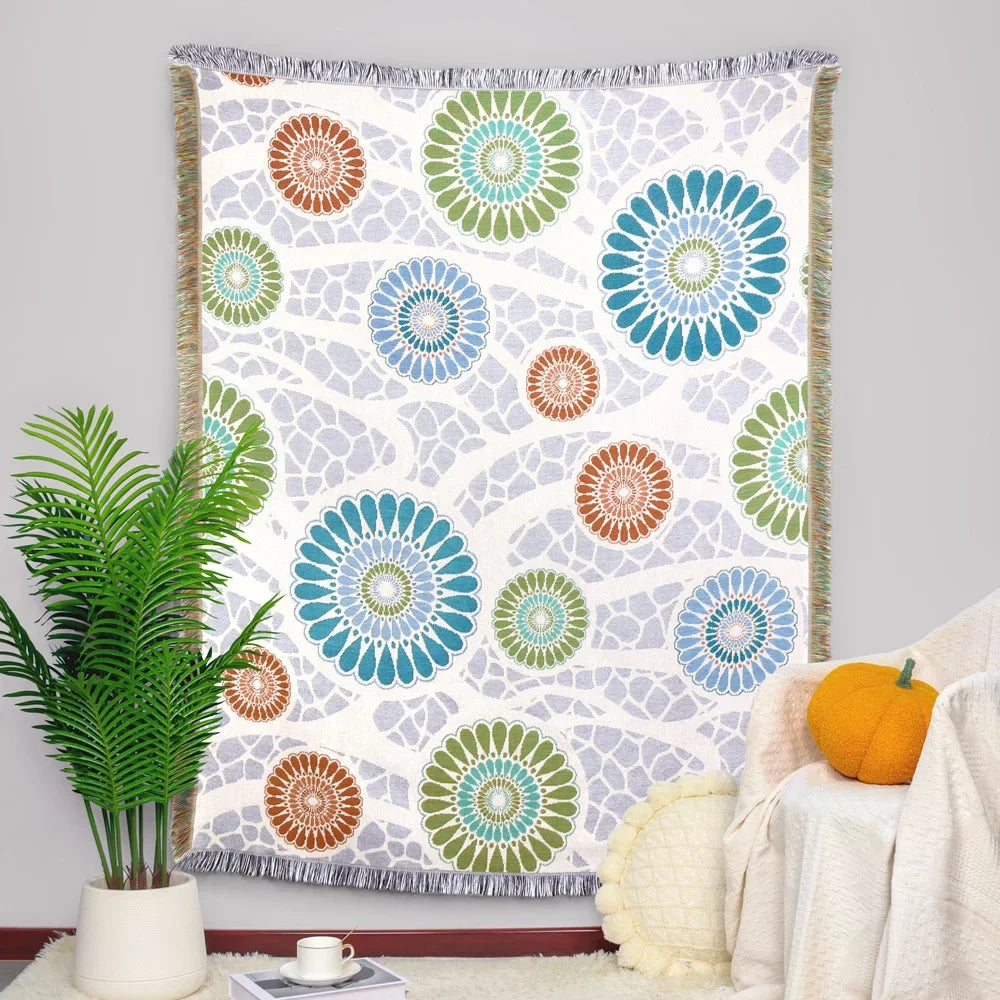 Une couverture décorative aux motifs floraux colorés et géométriques en tons pastels sur un fond blanc.