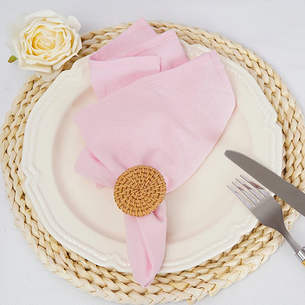 Sur un napperon en paille tressée, un serviette en rose et un élégant bouton de rose blanche sont disposés, créant une composition raffinée et harmonieuse.