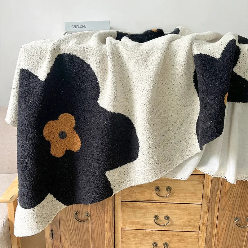 Couverture moelleuse à motifs floraux noirs et beiges, posée sur un meuble en bois, avec une étiquette indiquant "Geraldine".