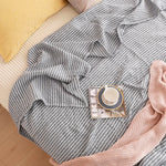 Élégante couverture grise rayée, posée sur un canapé beige, avec une tasse de café et un assortiment de coussins décoratifs.