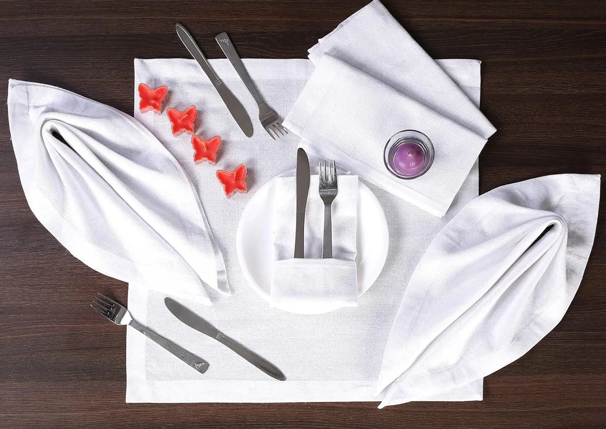 Couverts et serviettes blancs sur une table en bois foncé, avec de petites décorations rouges en forme d'étoiles.