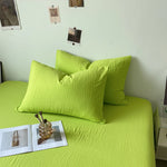 Ensemble de literie vert citron avec des coussins et des éléments décoratifs posés sur le lit.